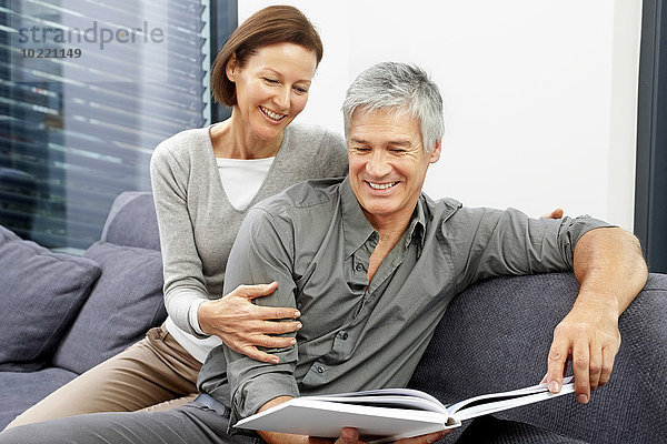Porträt eines glücklichen Paares  das zusammen auf der Couch sitzt und ein Buch betrachtet.