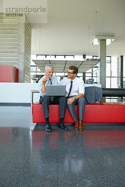 Zwei lächelnde Geschäftsleute bei der Arbeit am Laptop in der Bürolobby