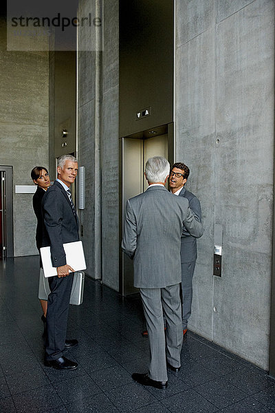 Gruppe von Geschäftsleuten im Gespräch an einem Aufzug im Büro