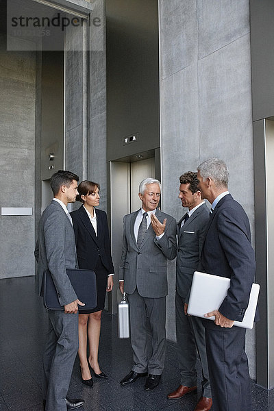 Gruppe von Geschäftsleuten im Gespräch an einem Aufzug im Büro