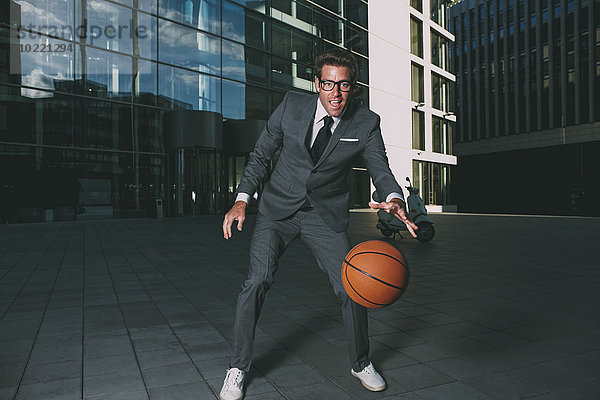Geschäftsmann spielt Basketball vor dem Bürogebäude