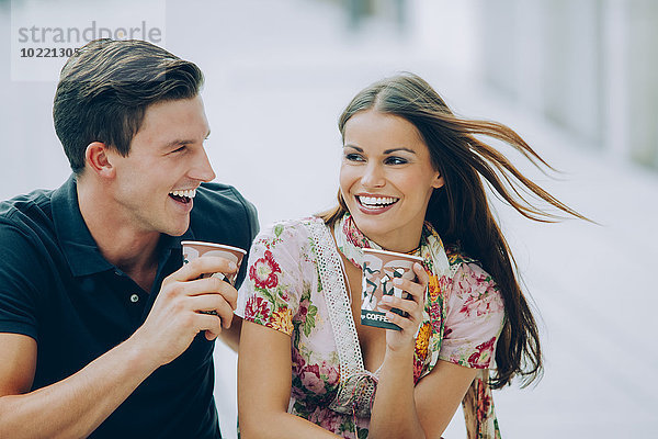 Fröhliches junges Paar trinkt Kaffee im Freien