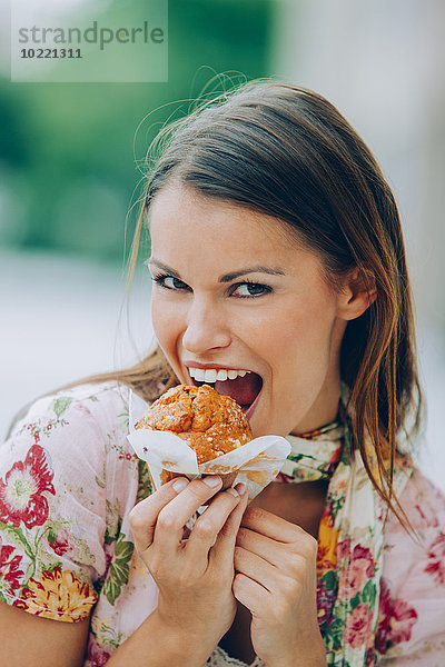 Fröhliche junge Frau beim Muffinessen im Freien