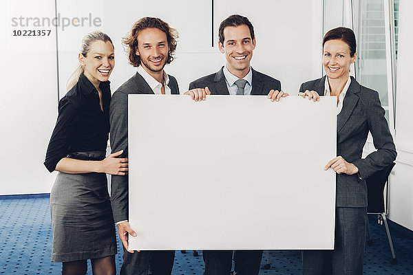 Porträt eines glücklichen Geschäftsteams mit einer leeren Plakatwand im Büro