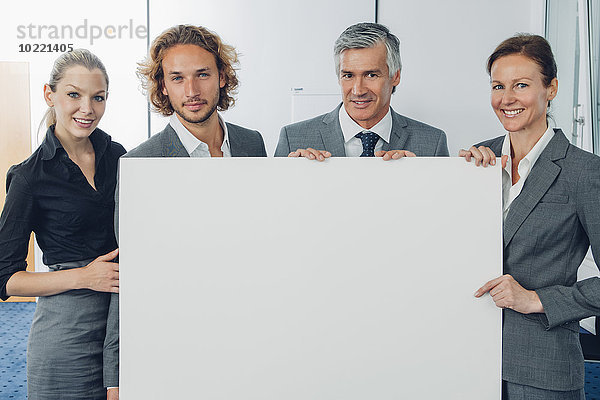 Porträt eines glücklichen Geschäftsteams mit einer leeren Plakatwand im Büro