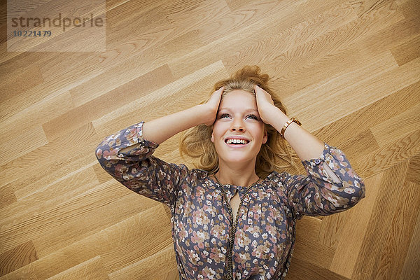Draufsicht einer lächelnden jungen Frau  die auf dem Boden liegt und ihren Kopf hält.