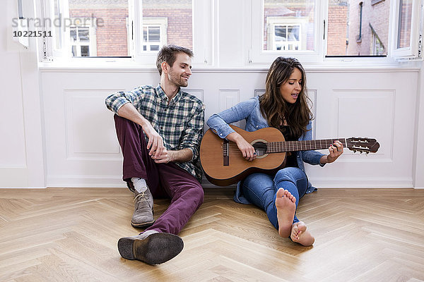 Junges Paar auf dem Boden sitzend mit Gitarrenspielerin