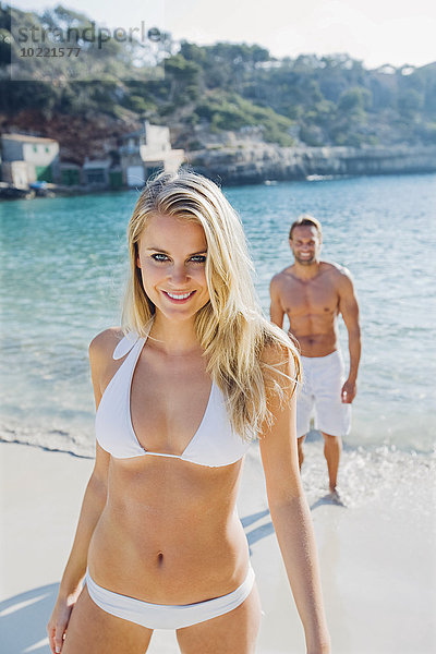 Spanien  Mallorca  lächelnde Frau im Bikini am Strand mit Mann im Hintergrund