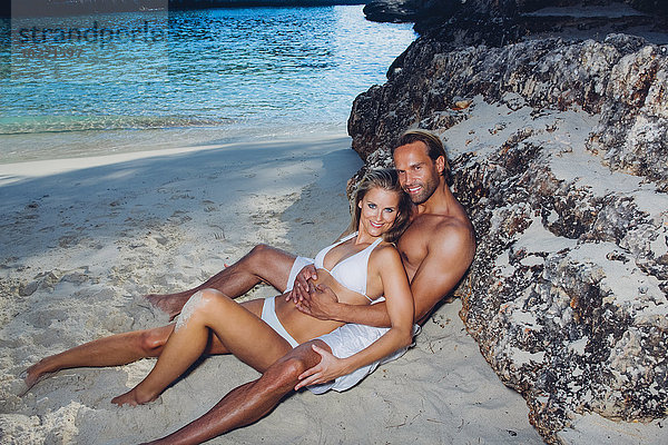Spanien  Mallorca  lächelndes Paar  das sich gegen einen Felsen am Strand lehnt