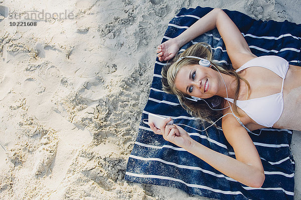 Lächelnde Frau beim Entspannen und Musik hören am Strand