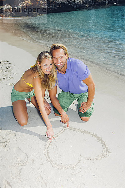 Verliebtes Paar am Strand zeichnet Herz im Sand