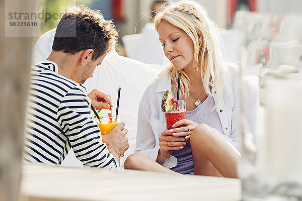 Junges Paar sitzt in einem Café im Freien mit Gläsern frischem Saft.