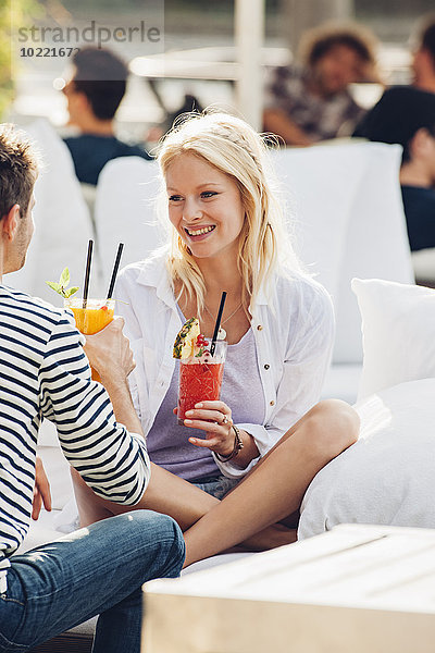 Porträt einer glücklichen jungen Frau mit einem Glas frischem Saft  die mit ihrem Freund in einem Straßencafé sitzt.