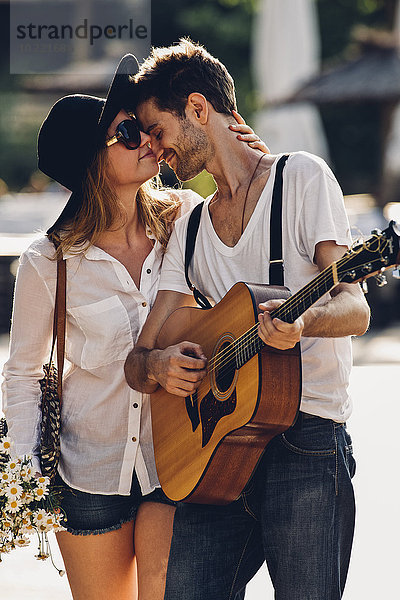 Liebevolles junges Paar mit Gitarre und Blumenstrauß