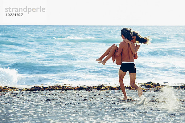 USA  Miami  junger Mann  der seine Freundin trägt und ins Meer rennt