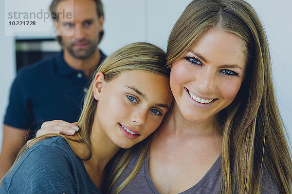 Porträt der lächelnden Mutter und Tochter mit Vater im Hintergrund