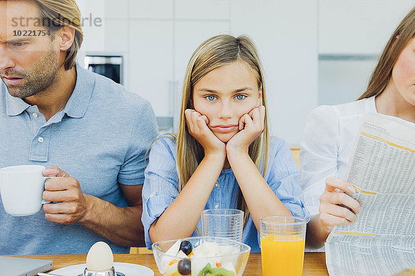 Frustriertes Mädchen mit abgelenkten Eltern am Frühstückstisch