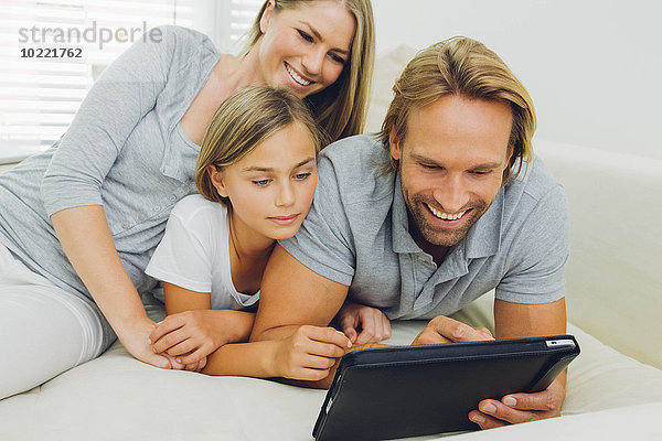 Glücklicher Vater  Mutter und Tochter liegen auf der Couch und teilen sich ein digitales Tablett.