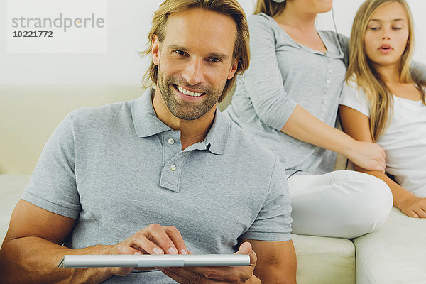Mann mit digitalem Tablett mit Frau und Mädchen im Hintergrund