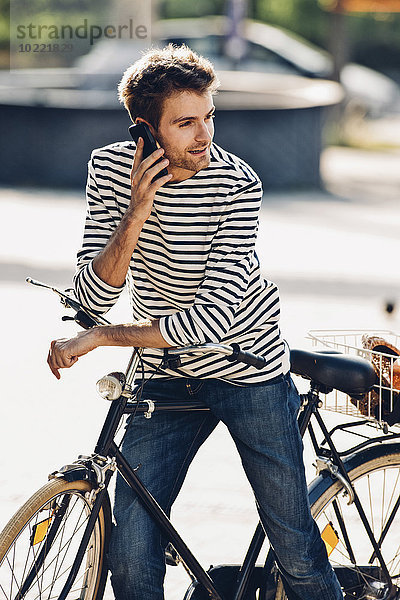 Junger Mann mit Fahrrad telefoniert mit seinem Smartphone