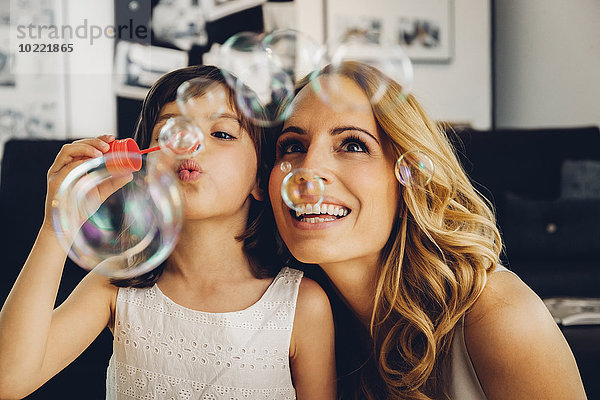 Glückliche Mutter mit Tochter zu Hause  die Seifenblasen bläst.