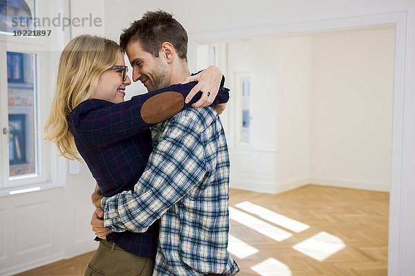 Glückliches junges Paar  das sich in einer leeren Wohnung umarmt.