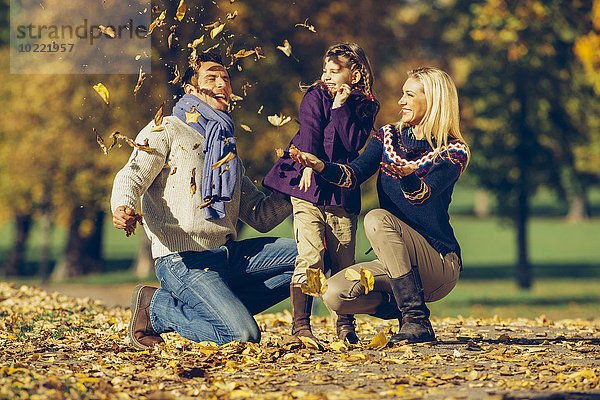 Eltern und Tochter beim Spielen mit trockenen Blättern im Park