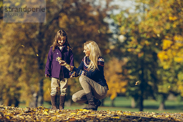 Mutter und Tochter beim Spielen mit trockenen Blättern im Herbstpark