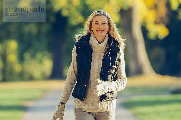 Porträt einer lächelnden Frau in warmer Kleidung beim Spaziergang im Park