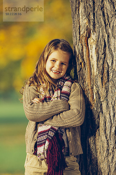 Porträt eines lächelnden Mädchens  das sich auf einen Baumstamm stützt.