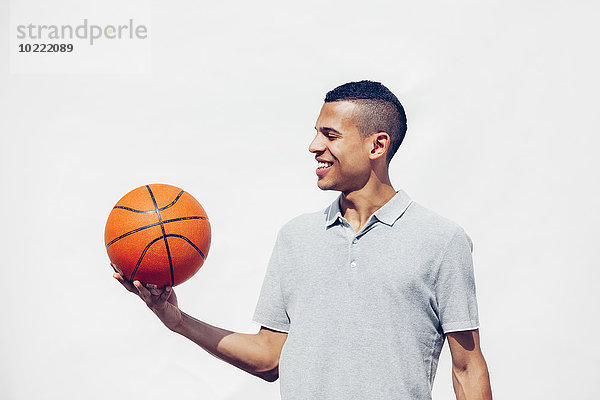 Portrait eines jungen Mannes mit rasiertem Haar  der Basketball vor weißem Hintergrund hält.