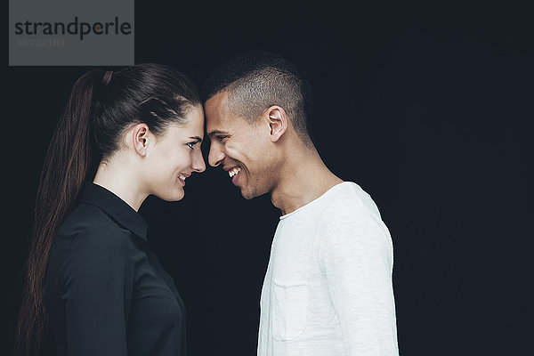 Glückliches junges Paar von Angesicht zu Angesicht vor schwarzem Hintergrund