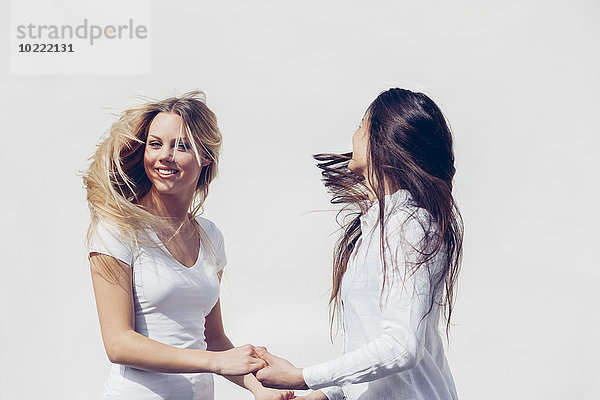 Zwei junge Frauen in weißer Kleidung  die ihre Haare vor weißem Hintergrund werfen.