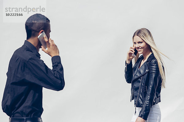 Zwei junge Leute telefonieren mit Smartphones  die sich gegenseitig beobachten.