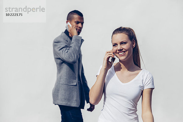 Porträt einer lächelnden jungen Frau beim Telefonieren mit dem Smartphone vor dem jungen Mann
