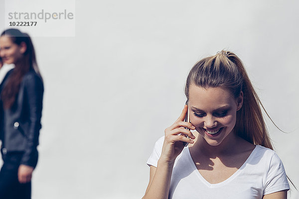 Porträt einer lächelnden jungen Frau beim Telefonieren mit Smartphone vor weißem Hintergrund