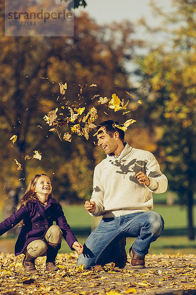 Porträt eines glücklichen Vaters und einer glücklichen Tochter  die mit trockenen Blättern in einem Park spielen.