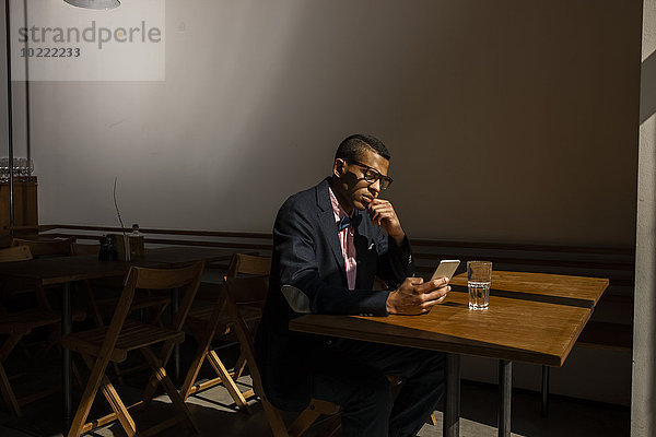 Junger Mann sitzt im Cafe  wartet auf jemanden  liest SMS