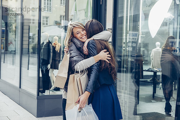 Zwei glückliche junge Frauen mit Einkaufstaschen  die sich vor einem Laden umarmen.
