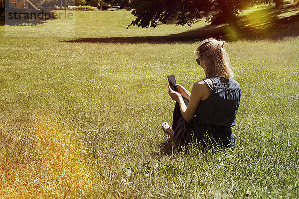 Frau sitzt auf der Wiese eines Parks mit dem Smartphone