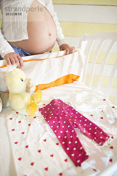 Schwangere Frau steht hinter einem Kinderbett