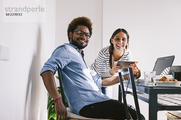 Lächelnder junger Mann und Frau bei der Arbeit mit Laptop und digitalem Tablett im Home Office