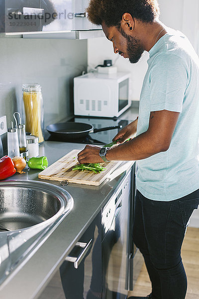 Junger Mann schneidet Gemüse in seiner Küche
