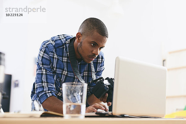 Junger Mann arbeitet mit Laptop in seinem Fotostudio