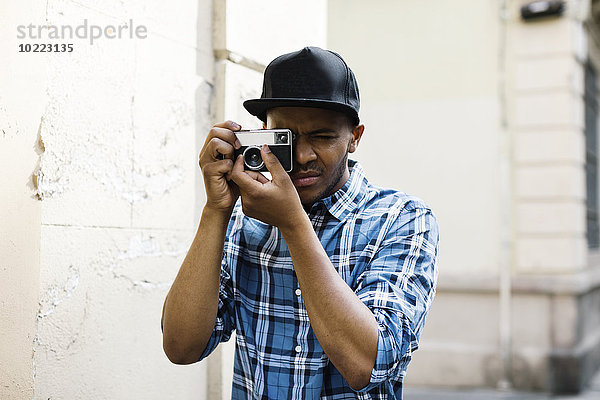 Junger Mann mit Baseballmütze und Kamera beim Fotografieren auf der Straße