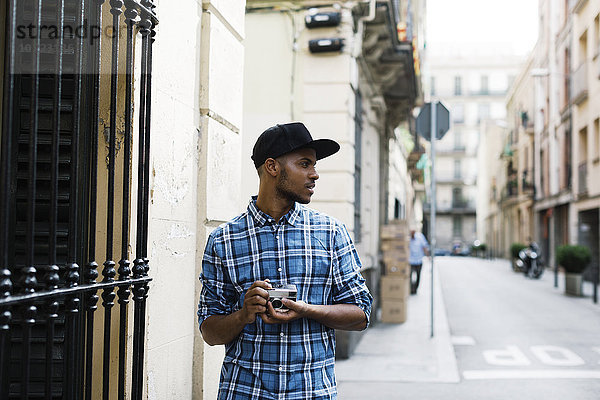Spanien  Barcelona  junger Mann mit Baseballmütze und Kamera auf der Straße