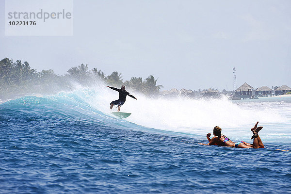 Malediven  Süd Male Atoll  Mann beim Surfen  während die Frau auf ihrem Surfbrett liegt und ihn beobachtet.