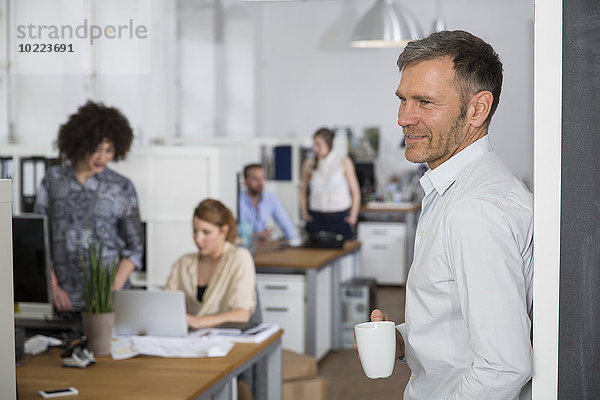 Lächelnder Mann im Büro mit Kollegen im Hintergrund