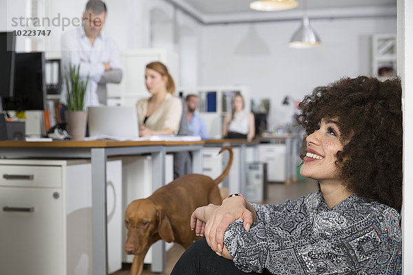 Lächelnde Frau im Büro mit Kollegen und Hund im Hintergrund