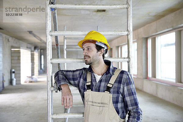Mann mit Schutzhelm auf der Baustelle denken